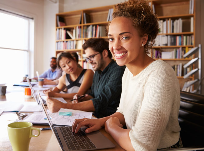 Businesswoman Using Laptop At Desk In Busy Office